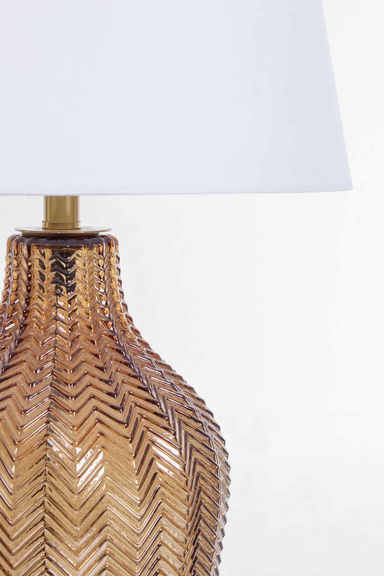 Die Tischleuchte Gleaming überzeugt mit ihrem klassischen Design. Gefertigt wurde sie aus Glas, welches einen braunen Farbton besitzt. Der Lampenschirm ist aus Terylen und hat eine weiße Farbe. Die Lampe besitzt eine Höhe von 62 cm.
