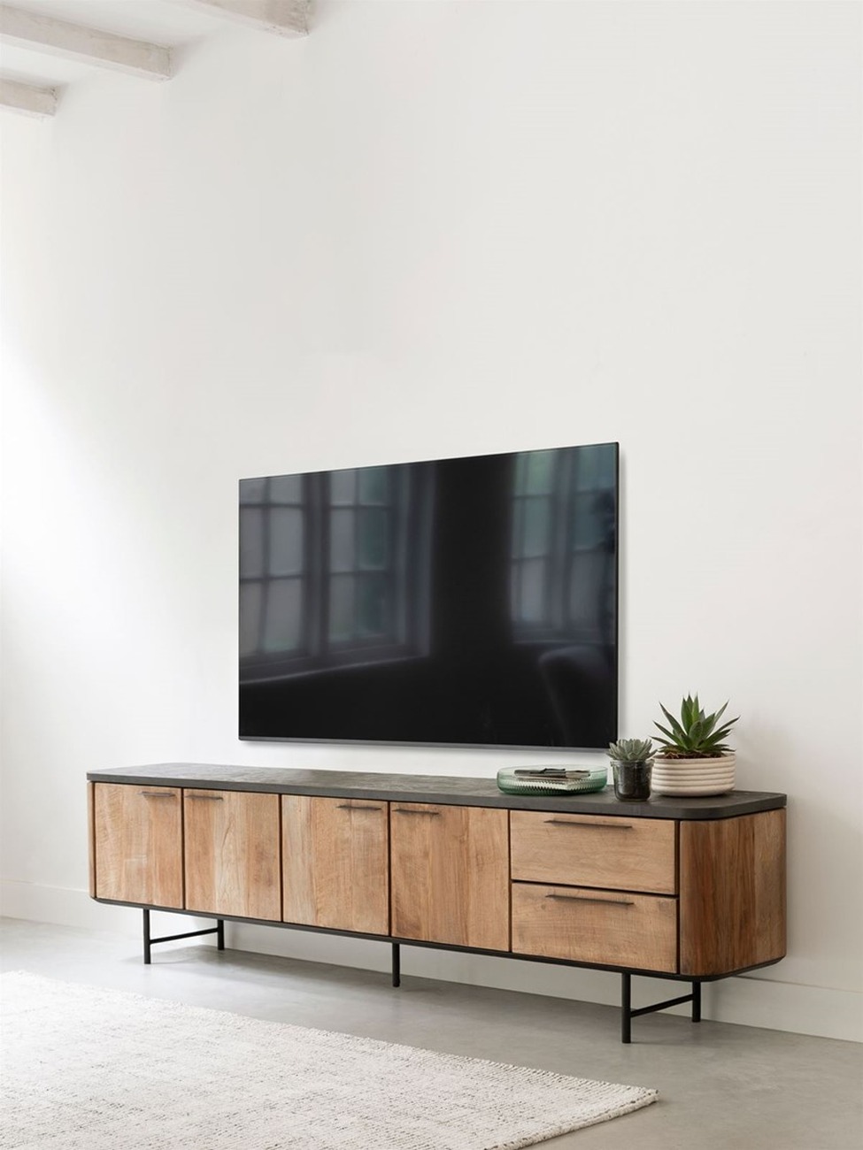 Das TV Board Soho überzeugt mit seinem modernen Design. Gefertigt wurde es aus recyceltem Teakholz, welches einen natürlichen Farbton besitzt. Das Gestell ist aus Metall und hat eine schwarze Farbe. Das TV Board besitzt eine Breite von 230 cm.